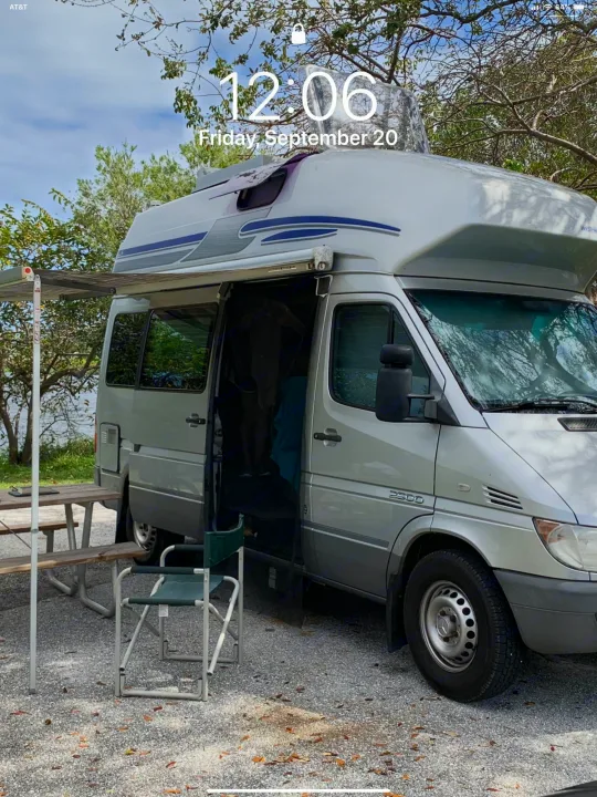 Silver Westfalia Sprinter RV rental parked at a serene lakeside campsite, with its awning extended and a picnic area.. Airstream Westfalia 2005