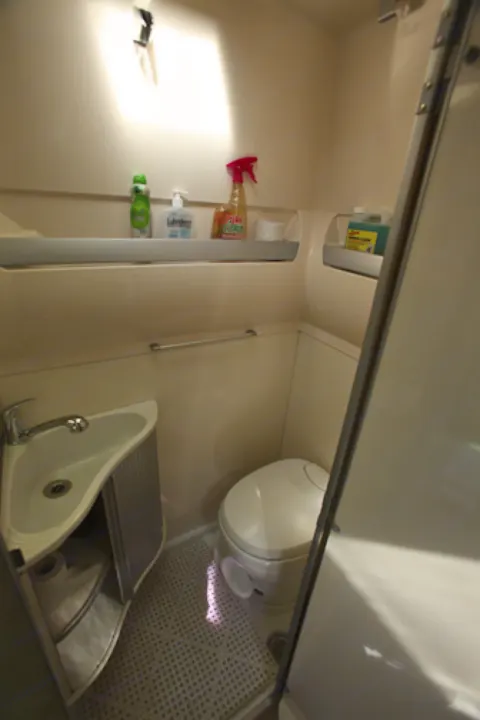 Compact RV rental wet bath with sink, toilet, and shower stall visible on a textured floor. Shelves hold toiletries.. Airstream Westfalia 2005