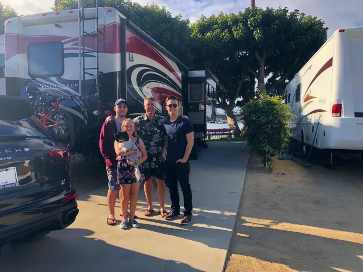 Family & dog pose by their RV rental, a Sightseer motorhome, at an RV park, with a Porsche & second RV nearby.. Winnebago Sightseer 2015