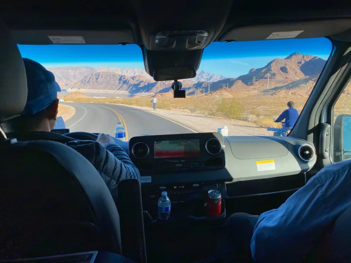 RV rental road trip: Driver's view of scenic mountains, a lake, and cyclists on the road ahead.. Winnebago Revel 2021