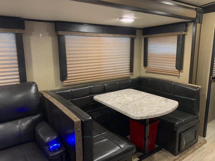 This RV rental features a modern interior with a black U-shaped dinette, light marble-look table, and blue-lit recliner.. Grand Design Imagine 2019