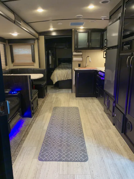 Bright RV rental interior: Modern kitchen, dining booth, and rear bedroom. Features accent blue lighting throughout.. Grand Design Imagine 2019