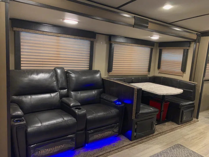 Inside an RV rental: black leather theater seating with blue LED accents, plus a compact dinette booth with large windows.. Grand Design Imagine 2019