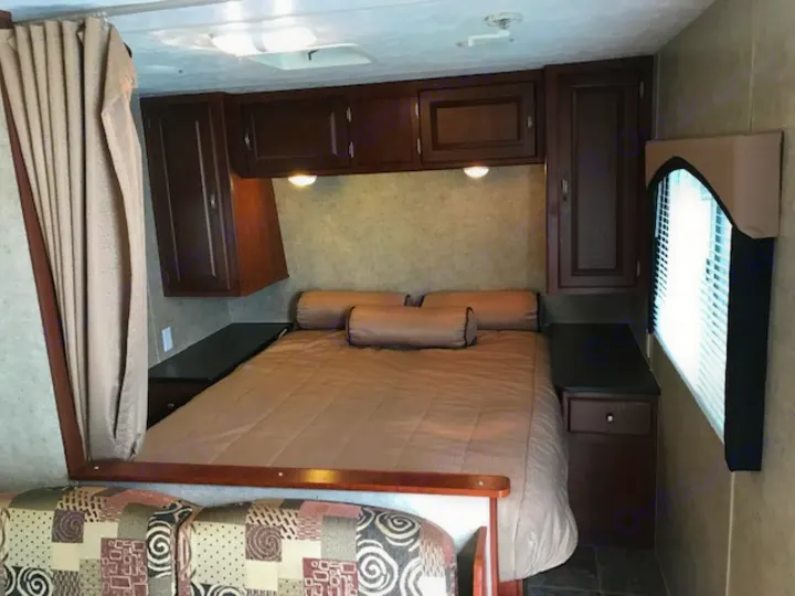 Inside an RV rental: a spacious bedroom with a comfy bed, dark wood cabinets, and a window for natural light.. Wildwood Wildwood 2011