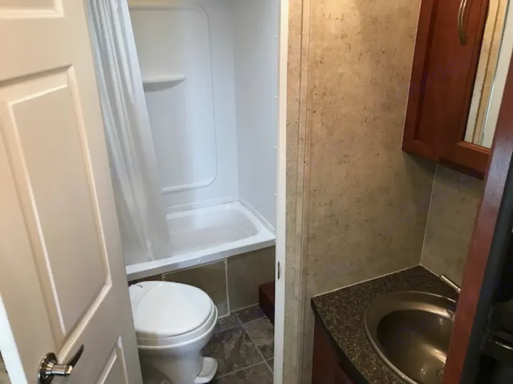 This RV rental bathroom features a toilet, compact shower/tub with curtain, and a small sink vanity on the right.. Wildwood Wildwood 2011