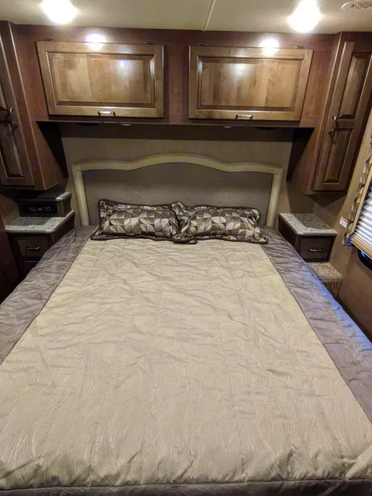 Comfortable RV rental bedroom with a large bed, patterned bedding, overhead cabinets, and built-in nightstands.. Other Hurricane 2017