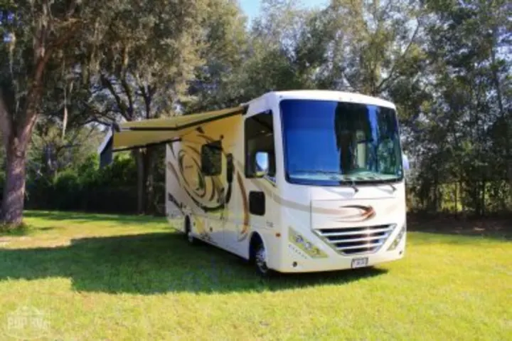 Cream-colored motorhome with awning extended, parked on green grass. Ideal for your next RV rental adventure.. Other Hurricane 2017