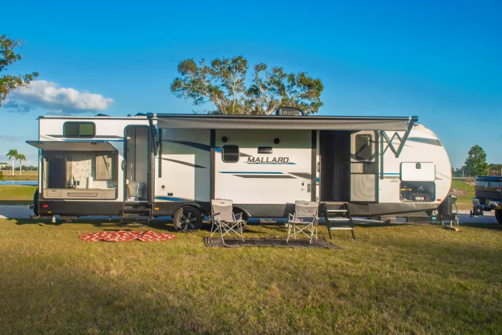 This RV rental features a full outdoor kitchen, extended awning, and camping chairs on a grassy site. Ready for adventure!. Heartland M-33 2021