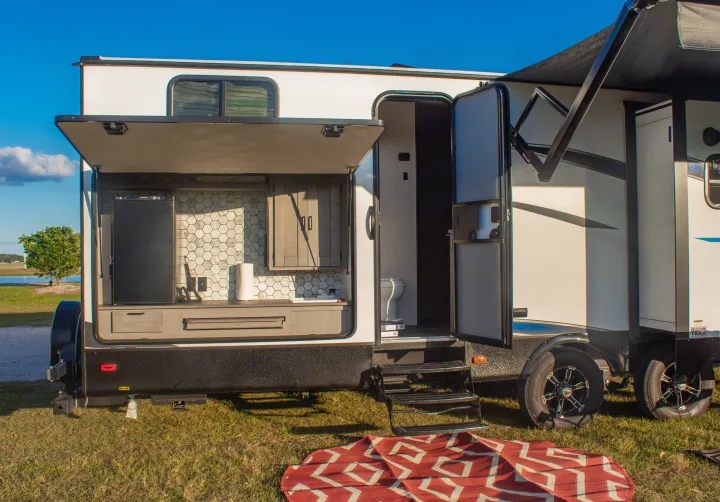 This RV rental showcases an open outdoor kitchen and an open interior door revealing a toilet. Perfect for travels!. Heartland M-33 2021