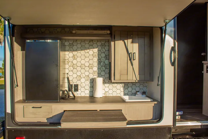 An RV rental outdoor kitchen with a large fridge, sink, hexagonal backsplash, and pull-out table. Perfect for adventures.. Heartland M-33 2021