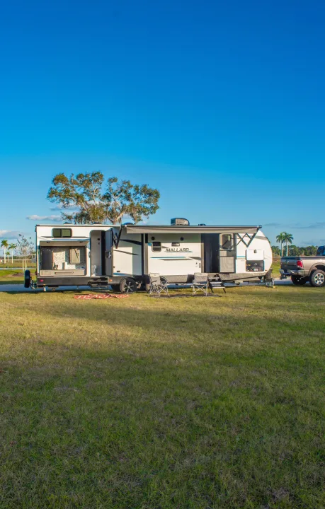 RV rental travel trailer set up at a sunny campsite with outdoor kitchen, awning, and chairs.. Heartland M-33 2021