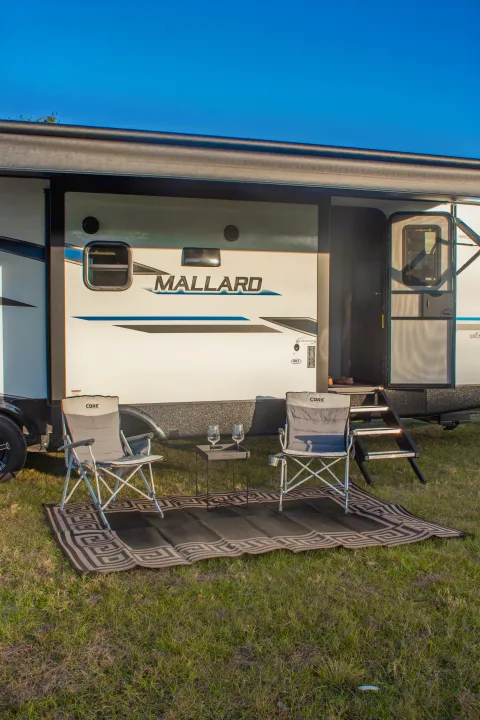 Relaxing RV rental setup: a Mallard camper, outdoor chairs, table, and rug ready for a peaceful evening.. Heartland M-33 2021