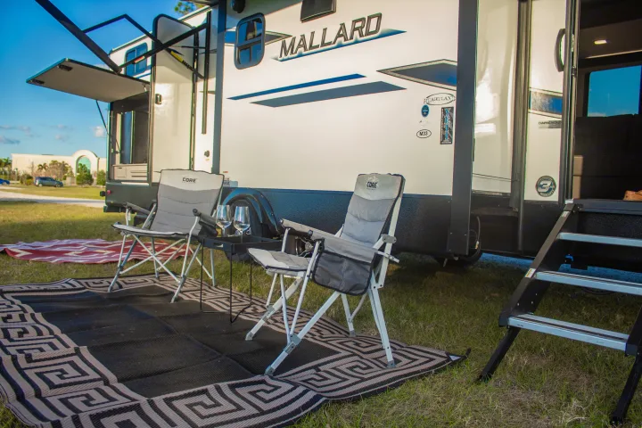 Relaxing rv rental campsite with comfy chairs & table on a patterned rug outside a Heartland Mallard RV.. Heartland M-33 2021