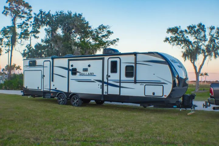 A modern white Mallard travel trailer, ideal for an RV rental adventure, parked on green grass with trees.. Heartland M-33 2021