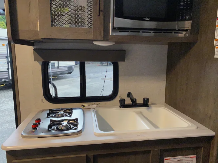 Compact kitchen inside an RV rental, featuring a two-burner stove, double sink, and microwave for travelers.. Forest River Wildwood Sport 2021