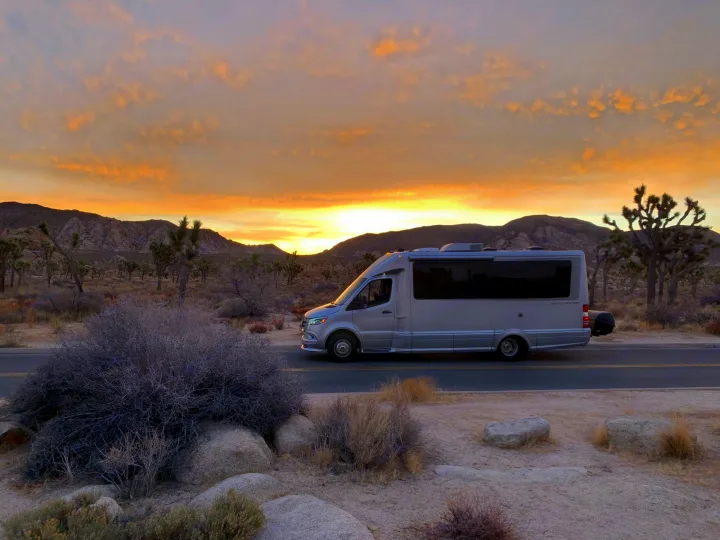 Sleek RV rental on a desert road at golden hour. See Joshua Trees and mountains. Plan your adventure road trip.. Airstream Atlas 2021