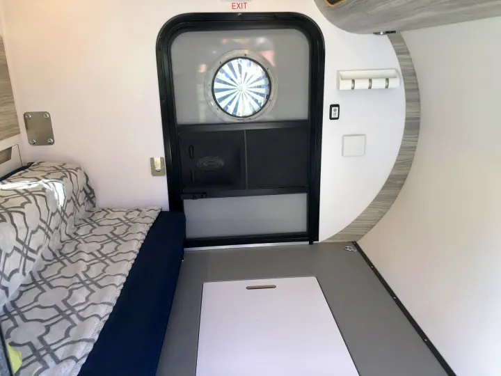 Experience RV rental comfort: interior shows bed, door with porthole, and floor panel in a compact camper.. Bean Trailer Mean 2020