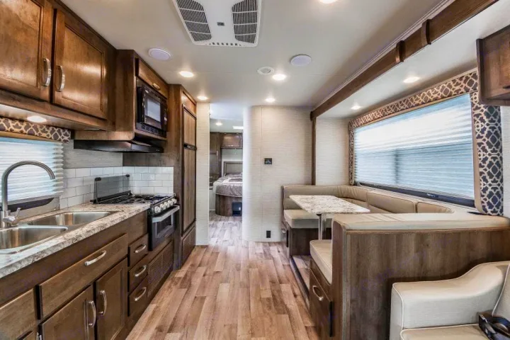Interior of a modern RV rental: features a fully equipped kitchen, spacious dining booth, and view towards the bedroom area.. Jayco Redhawk 2021