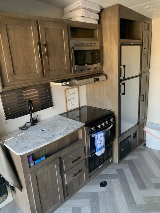 Modern RV rental kitchen featuring wood-look cabinets, a compact sink, microwave, stove, and refrigerator.. Forest River Salem Cruise Lite 2020