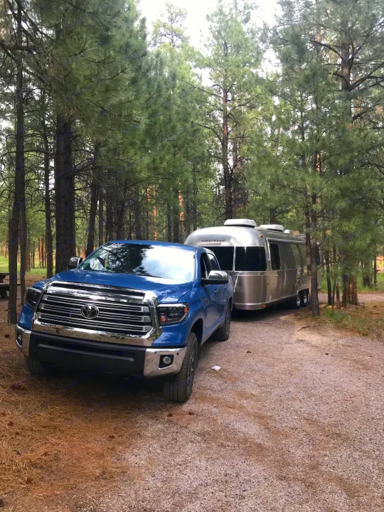 Blue truck and Airstream RV rental in a serene pine forest campsite. Perfect for your next adventure!. Airstream International 2014