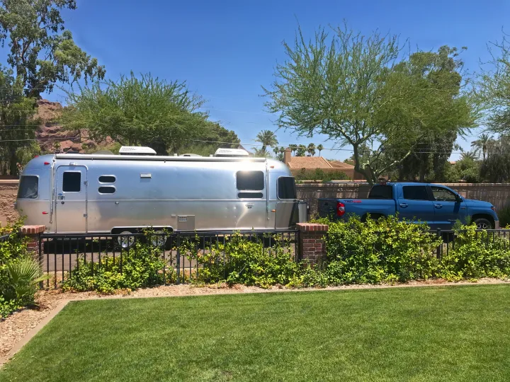 Shiny Airstream RV & blue pickup truck on a sunny day, ideal for an rv rental. Green lawn & desert landscape are visible.. Airstream International 2014