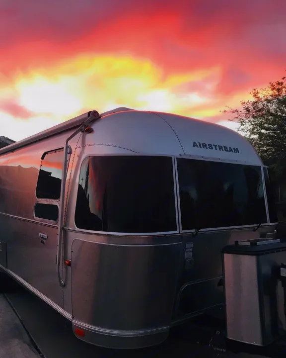 A gleaming silver Airstream travel trailer RV rental reflecting a vibrant pink and orange sunset sky. Your next adventure awaits!. Airstream International 2014