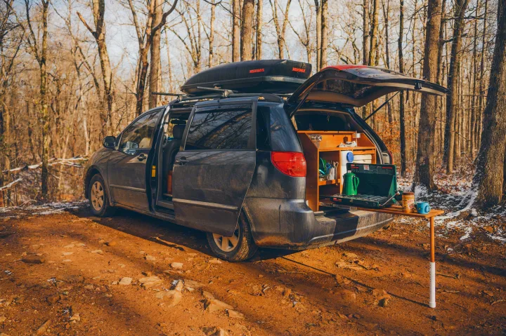 This customized minivan RV rental has its rear kitchen open in a winter forest, ready for cooking on a camping trip.. Toyota Other 2007