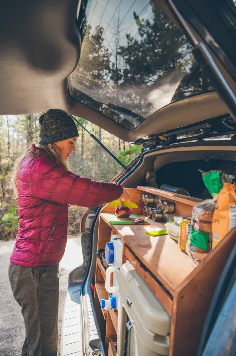 Woman prepares food in a custom RV rental kitchen, ideal for van life camping. Features a built-in mobile cooking station.. Toyota Other 2007