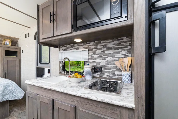 Step inside this cozy RV rental with a well-equipped kitchen: sink, stovetop, microwave, and stylish backsplash.. Gulf Stream Amerilite 2021