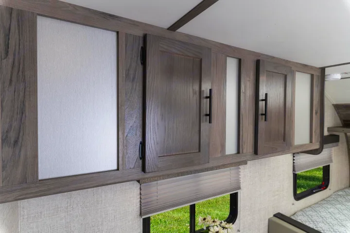 RV rental bedroom interior featuring modern woodgrain overhead cabinets, windows, and blinds.. Gulf Stream Amerilite 2021