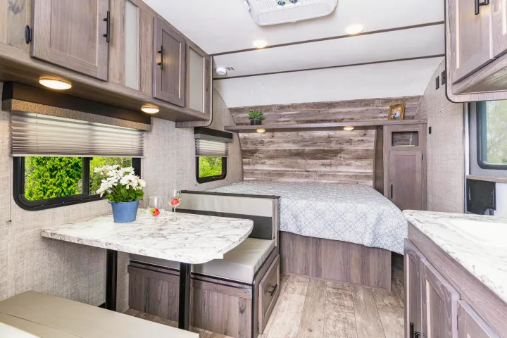 Modern RV rental interior showcasing a cozy dinette, comfortable bed, and functional kitchen cabinets for travel.. Gulf Stream Amerilite 2021