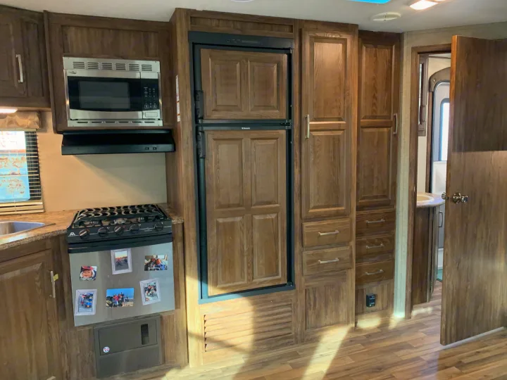 An RV rental's modern kitchen: wood cabinets, stainless microwave, stove, fridge, and sink area.. Keystone Cougar Half-Ton 2017