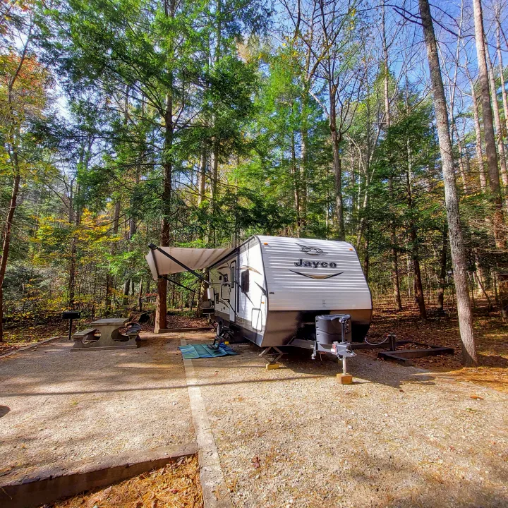 White RV rental parked at a forest campsite with a picnic table & grill under autumn trees.. Jayco Jay Flight SLX 2018