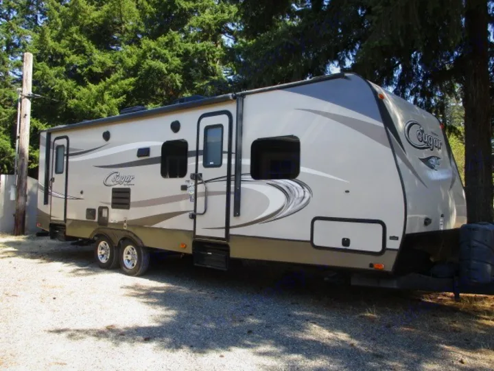 A beige Cougar travel trailer parked on gravel. This spacious RV rental is perfect for your next outdoor adventure.. Keystone Cougar Half-Ton 2017