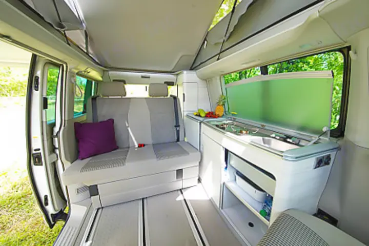 This rv rental camper van interior features a rear bench seat, kitchen with sink & stove, and pop-top roof for your adventures.. Volkswagen California Coast T6.1 DSG7 2023