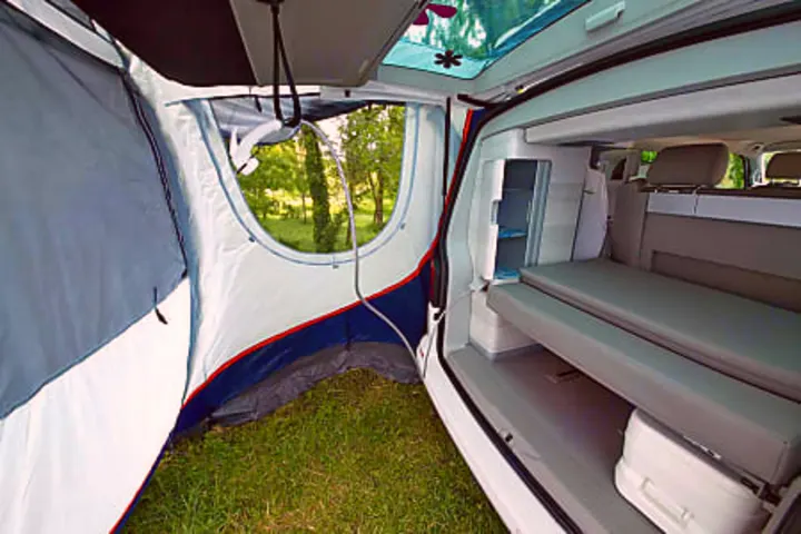 RV rental adventure awaits: camper's modular interior with bed, fridge, and attached tent annex, set on a grassy campsite.. Volkswagen California Coast T6.1 DSG7 2023