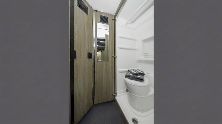 Compact **RV rental** bathroom with a shower stall, toilet topped with towels, and a wooden door featuring a mirror.. Winnebago Solis 2021