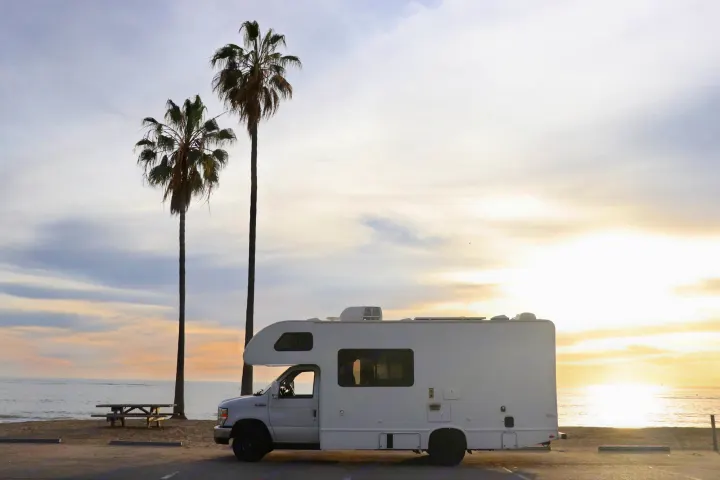This white RV rental enjoys a stunning beach sunset with palm trees. Perfect for your next adventure!. Thor Four Winds 2019