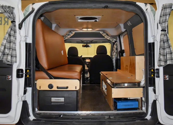 Inside an RV rental: Compact campervan conversion showing a brown bench-bed, Dometic fridge, and a functional kitchen.. Dodge Promaster City 2020