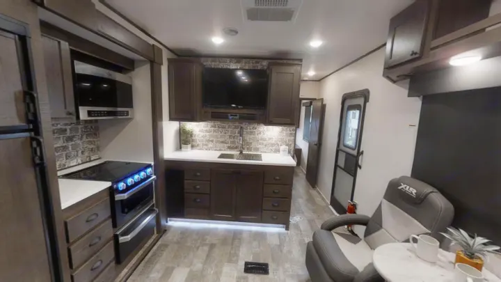 Spacious RV rental with a modern kitchen, dark wood cabinets, TV, and comfortable armchair seating.. Forest River XLR HYPERLITE 2815 2021