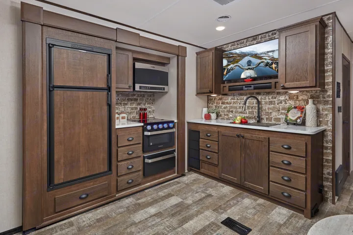 RV rental kitchen interior: modern wood cabinets, fridge, stove, microwave, sink, and mounted TV.. Forest River XLR HYPERLITE 2815 2021