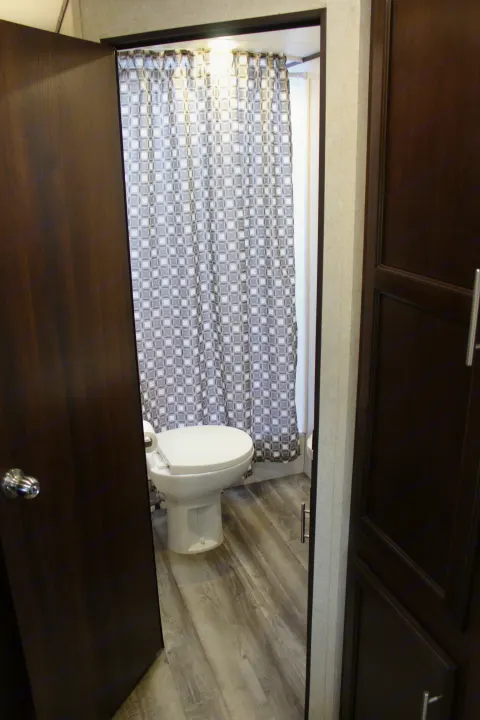 This RV rental bathroom features a white toilet, patterned shower curtain, and wood-look flooring.. Jayco Jay Flight SLX Rocky Mtn Edition 2019