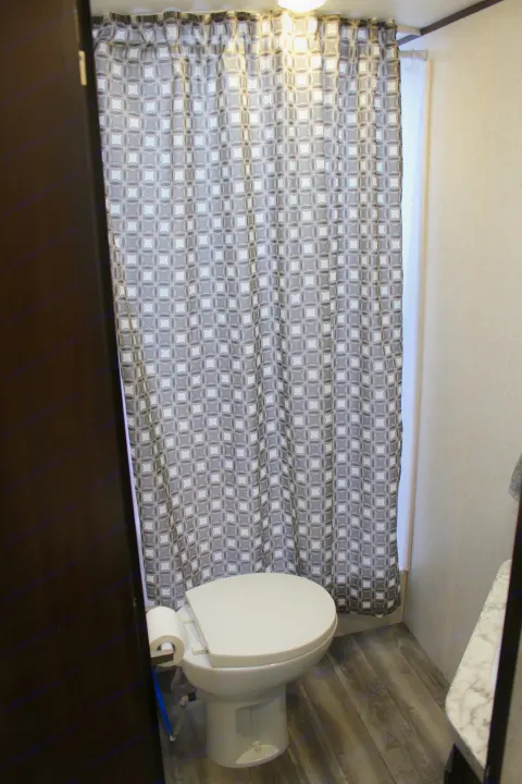 Compact RV rental bathroom: features a white toilet, geometric shower curtain, and wood-look floor.. Jayco Jay Flight SLX Rocky Mtn Edition 2019