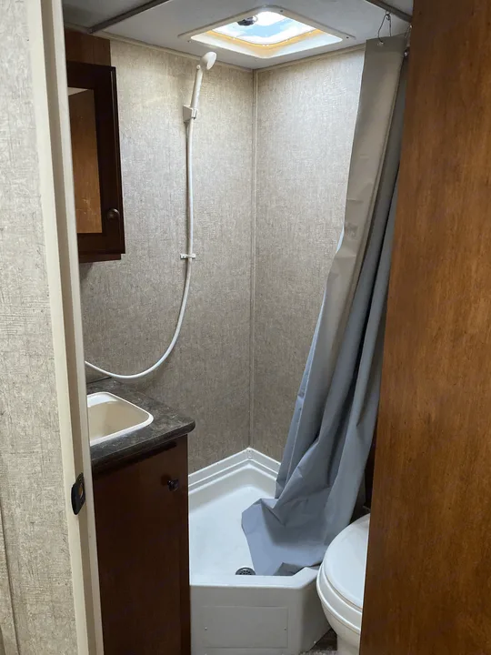 Compact RV rental bathroom: a corner shower with skylight, small sink vanity, and toilet for travelers.. K-Z Manufacturing Sportsman Classic 2015
