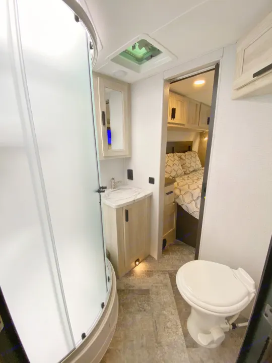RV rental interior: compact bathroom with shower, toilet, and sink vanity. Adjoining bedroom visible through the doorway.. Forest River Forester 2021