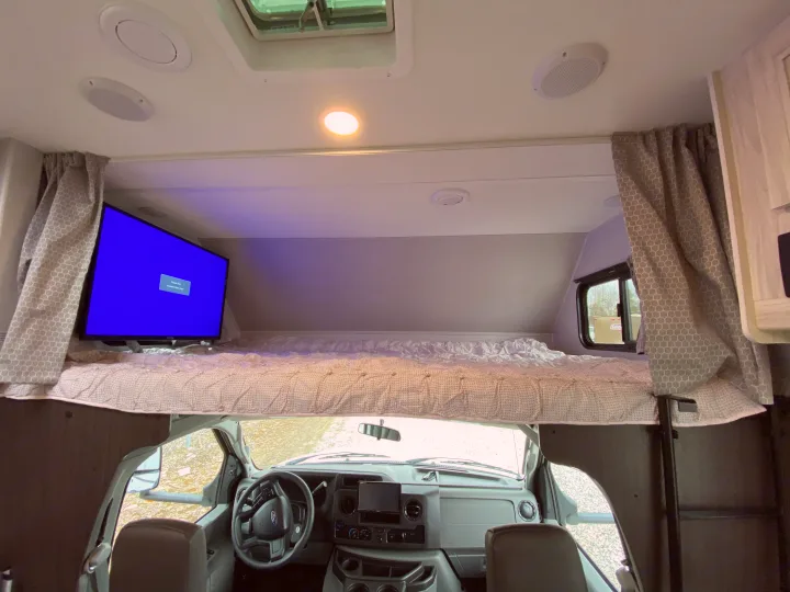 RV rental interior: A view of the cab-over bunk bed with a TV, positioned above the vehicle's dashboard and steering wheel.. Forest River Forester 2021