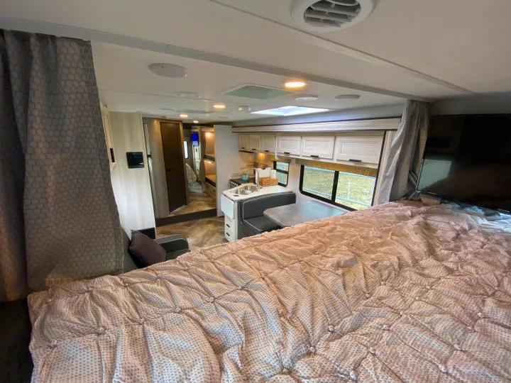 Cozy RV rental interior featuring a large bed, kitchen, dinette, and a view into the rear bunk and bath area.. Forest River Forester 2021