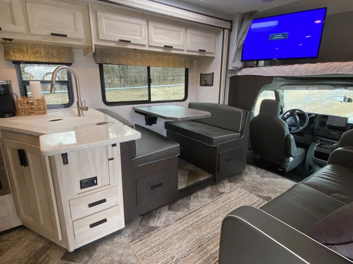 Spacious RV rental interior with a functional kitchen, dining booth, and living area with a TV, ideal for travel.. Forest River Forester 2021