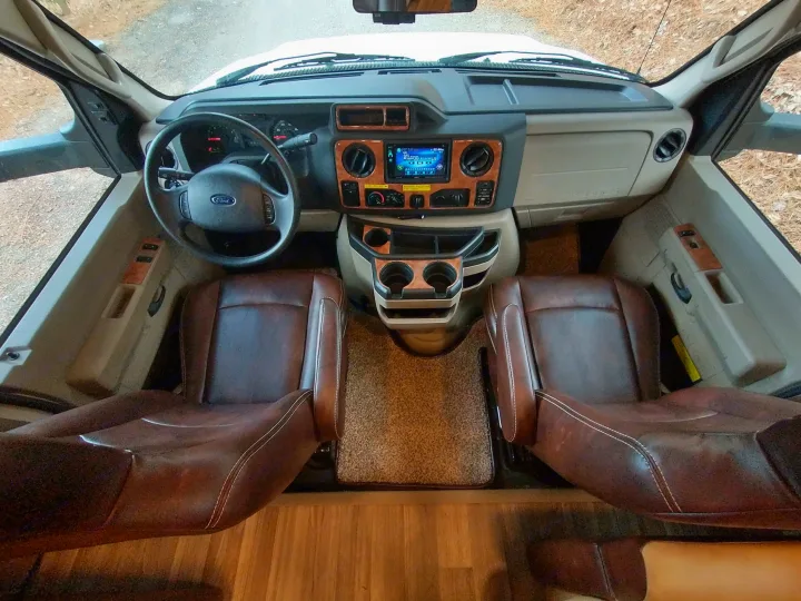 Inside an RV rental: View of a modern RV cockpit. Features brown leather seats, a Ford steering wheel, and a comprehensive dashboard.. Thor Quantum 2017