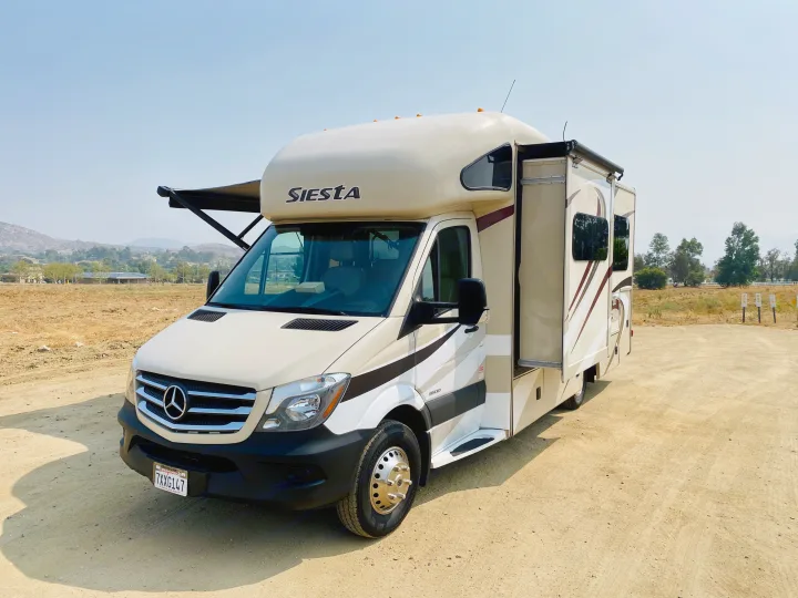 A beige Siesta RV rental, a Mercedes-Benz motorhome, parked on a dirt lot. Ready for adventure!. Thor Motor Coach Siesta 2017